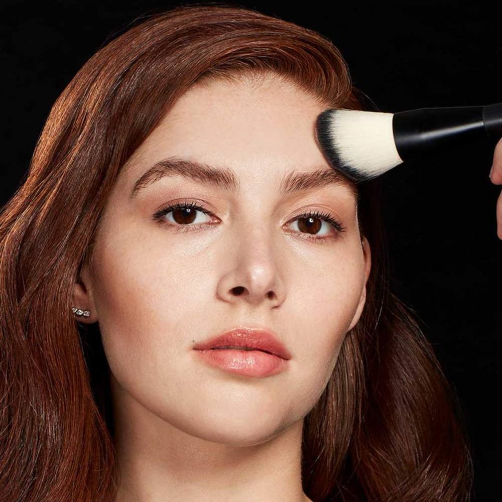 Woman applying powder on her cheek with a brush
